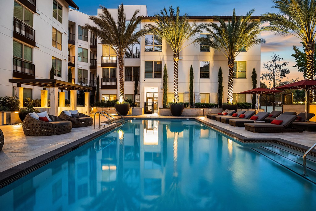 Twilight poolside view with glowing water, lush landscaping, and stylish lounge seating for relaxation