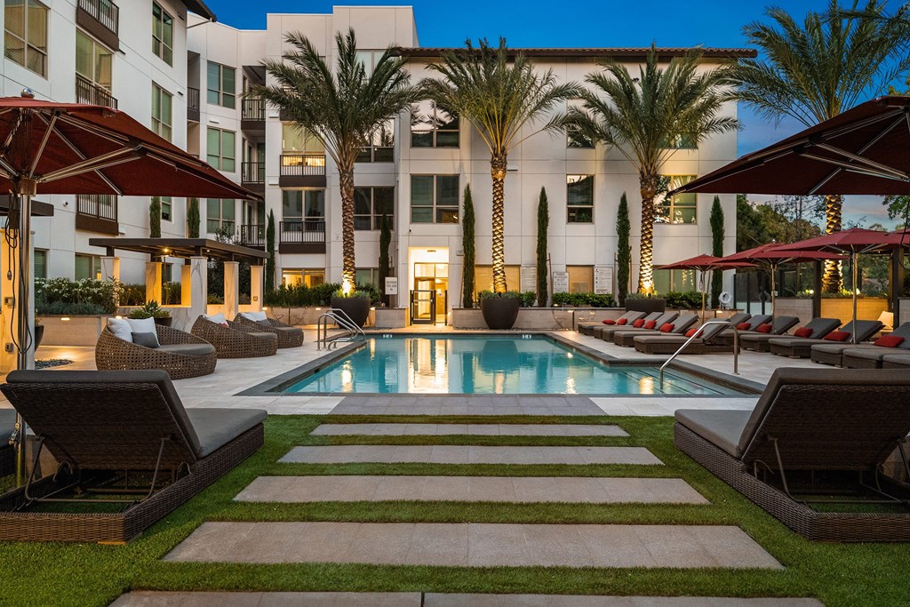 Evening pool deck with illuminated palm trees, cushioned loungers, and a tranquil resort-style atmosphere
