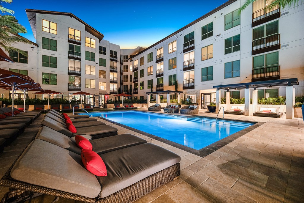 Sparkling pool lit at night, framed by red umbrellas and cushioned loungers for a true resort-style escape