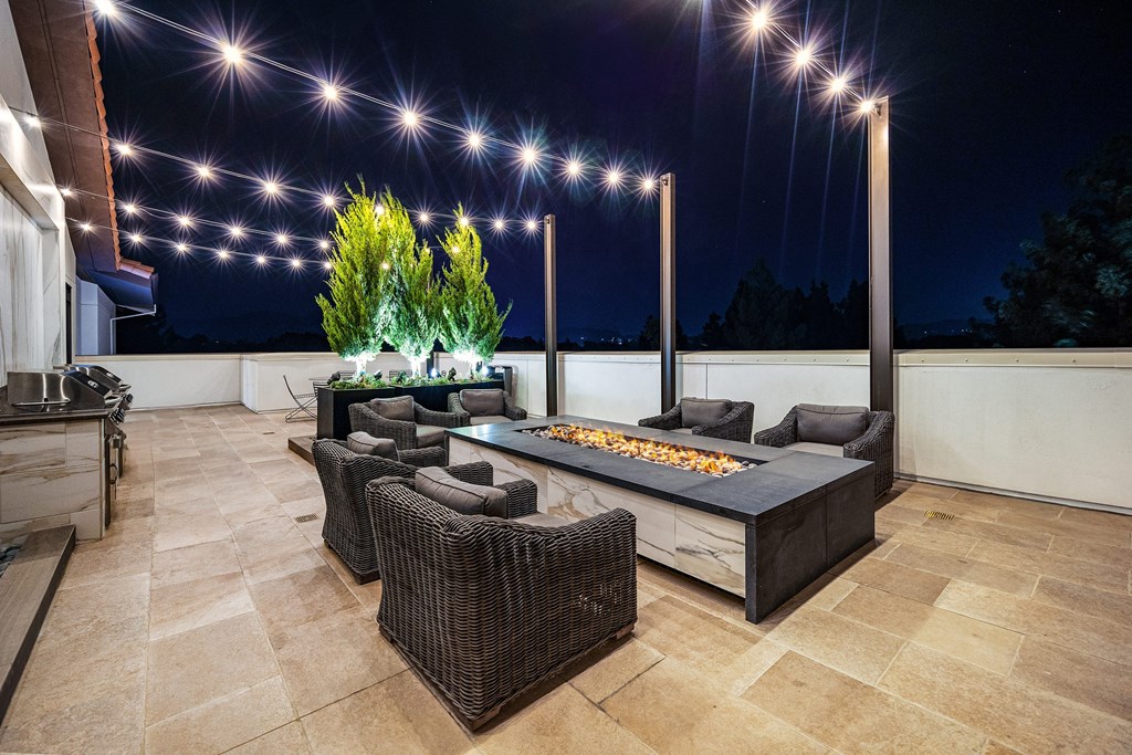 Rooftop terrace with fire pit lounge, string lights, and plush seating designed for cozy evenings