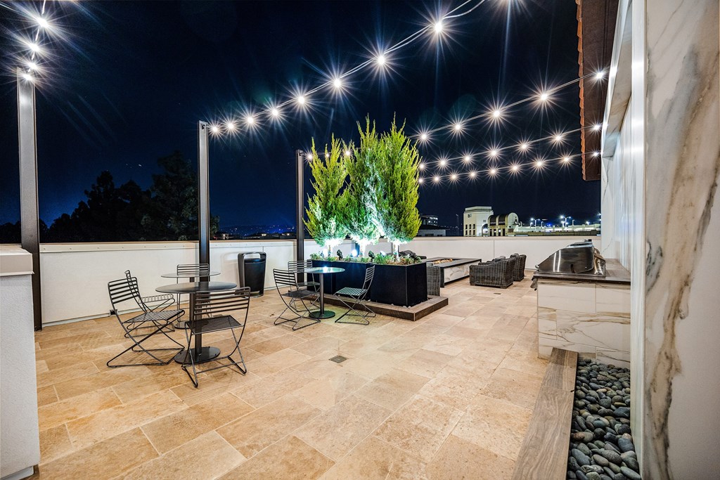 Rooftop terrace with fire pit lounge, string lights, and plush seating designed for cozy evenings