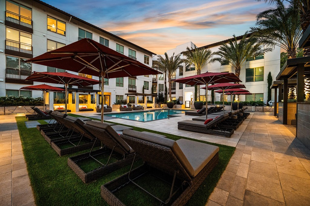 Poolside retreat with red umbrellas, plush loungers, and a glowing sunset backdrop
