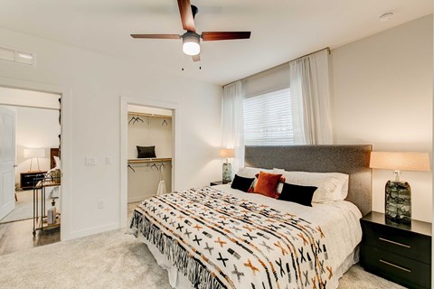 Bedroom with upholstered bed, ceiling fan, window, and open walk-in closet.