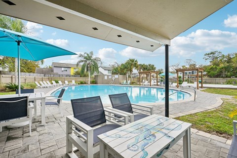 A poolside table with chairs and umbrellas overlooking a pool.