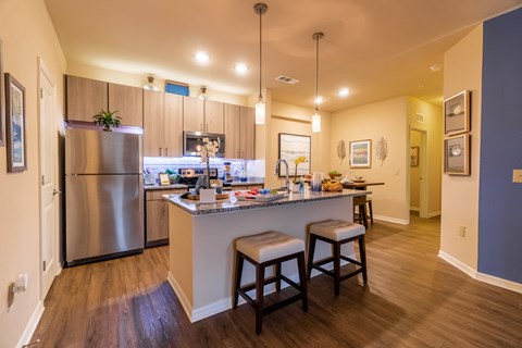 A kitchen with a refrigerator, island, and bar stools.