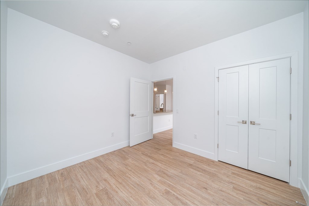 A room with white walls and wooden flooring with a door on the right.