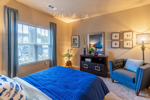 A bedroom with a blue bedspread and a blue chair.