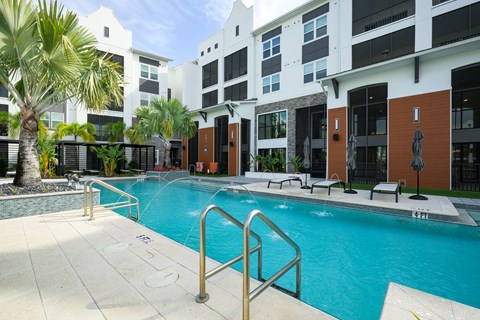 A swimming pool in front of a building with a palm tree.