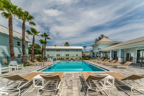 A pool surrounded by lounge chairs and palm trees.