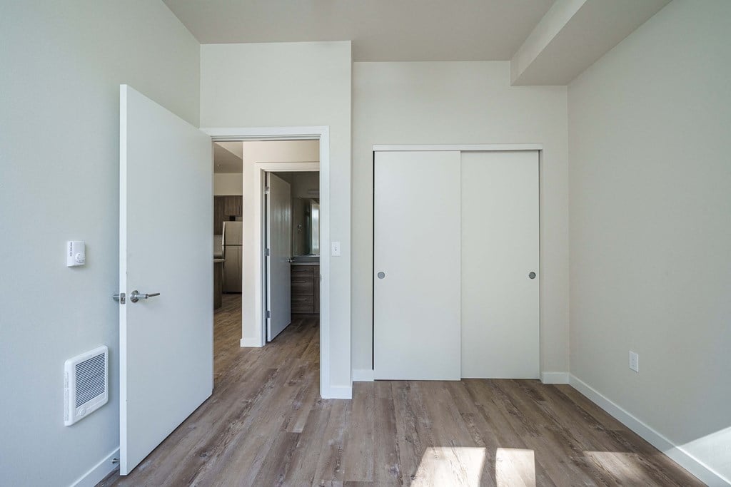 an empty living room with a door to a closet and a hallway to a bedroom