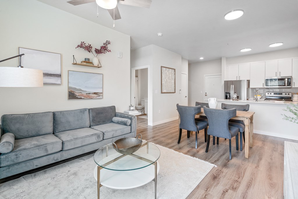 a living room with a couch a table and chairs and a kitchen in the background