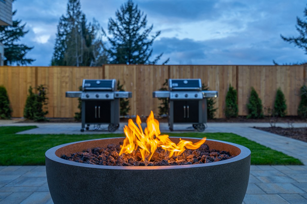 a fire pit in a backyard with two bbq grills in the background