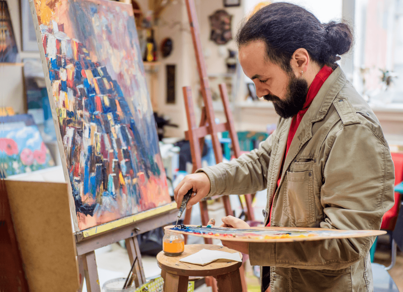 A man with a beard is painting a picture on a canvas.