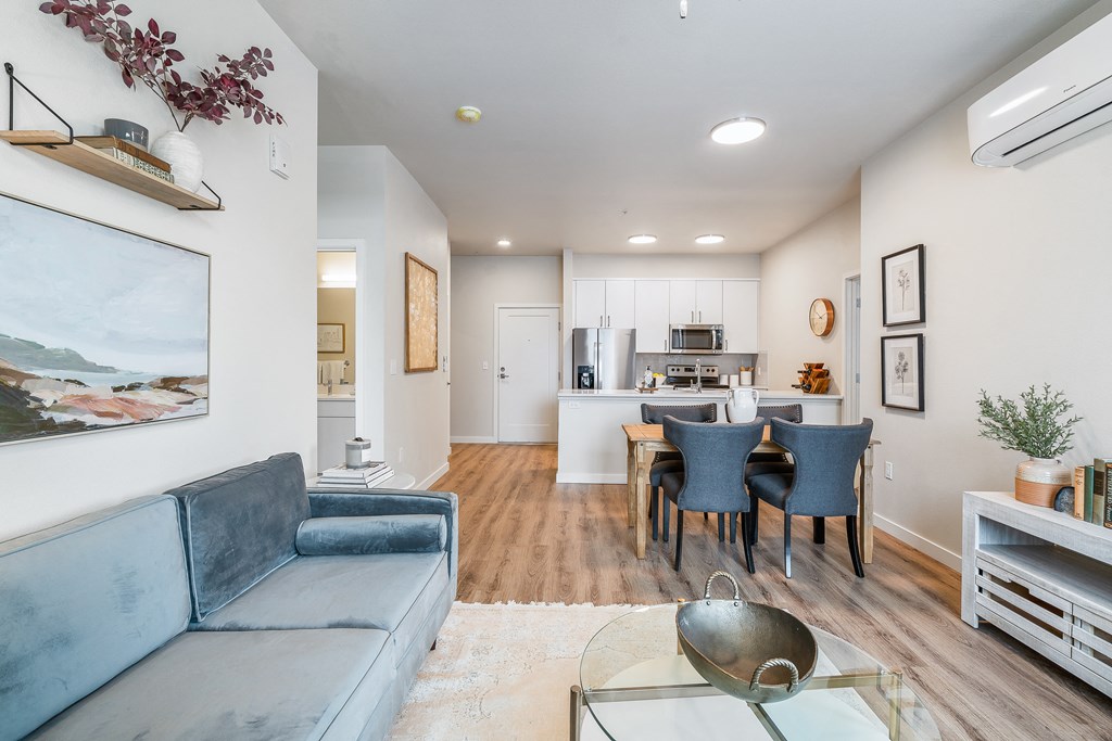 a living room with a couch a table and chairs and a kitchen in the background