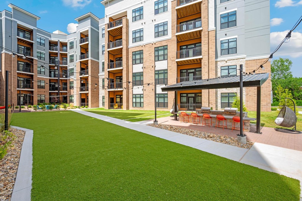 A modern apartment complex with a well-maintained lawn and outdoor seating area.