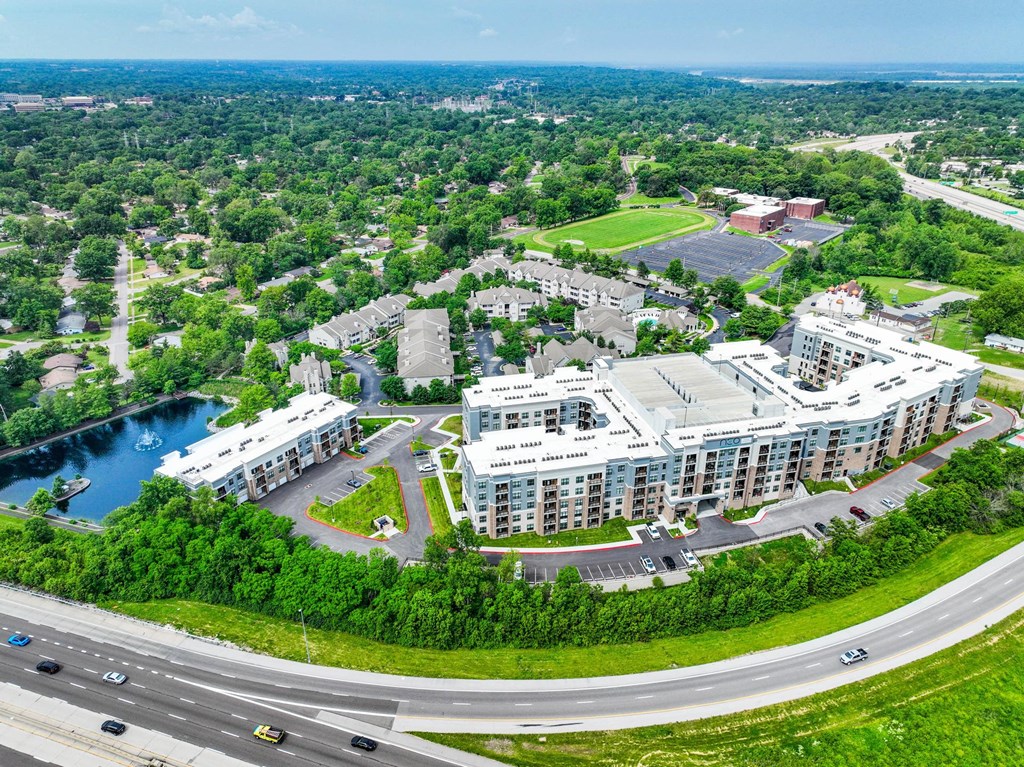 A large building complex is surrounded by a green landscape and a body of water.