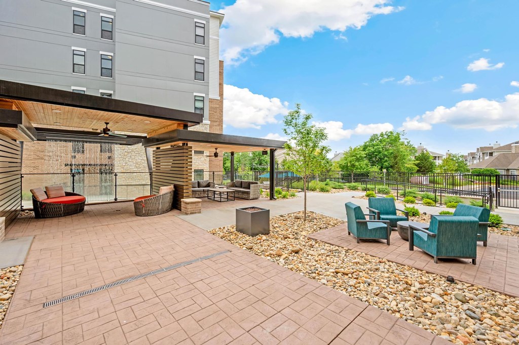 A patio area with a table and chairs is surrounded by a gravel bed and a fence.