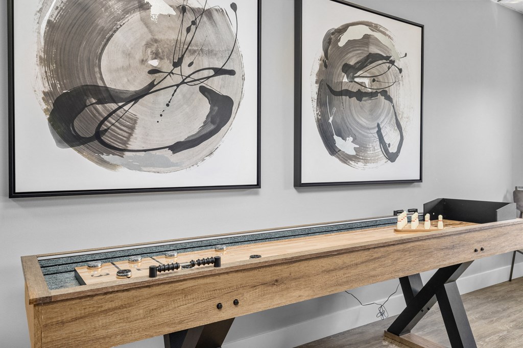 a game room with two large paintings on the wall and a shuffleboard table in the foreground