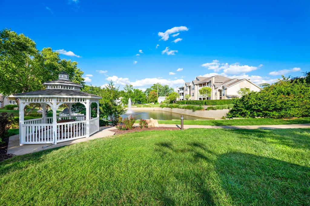 a gazebo sits in the middle of a grassy area next to a pond