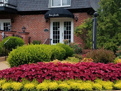 a garden in front of a brick house with a black umbrella on top