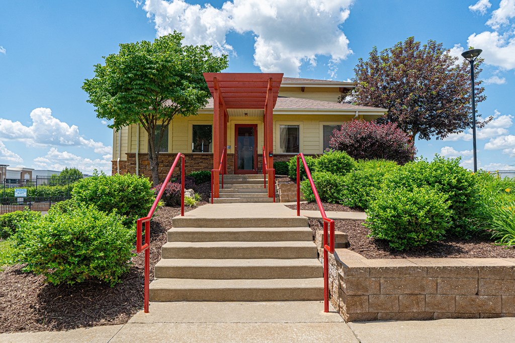 the front of a yellow house with red railings and stairs