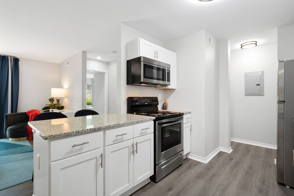 a kitchen with white cabinetry and a counter top with a stove and a microwave