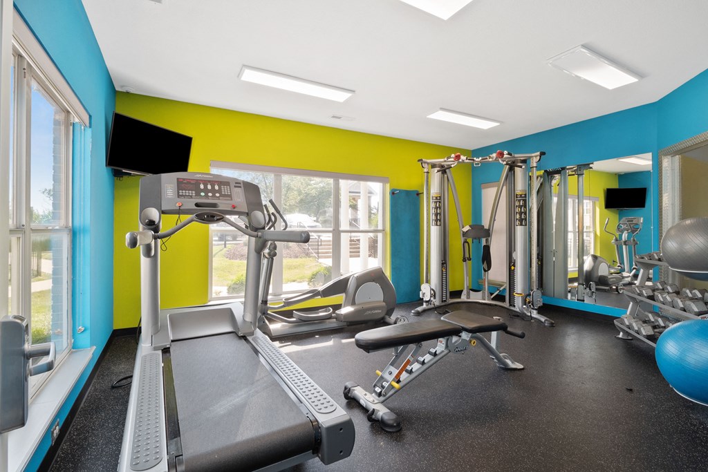 a gym with cardio equipment and weights in a building with yellow and blue walls