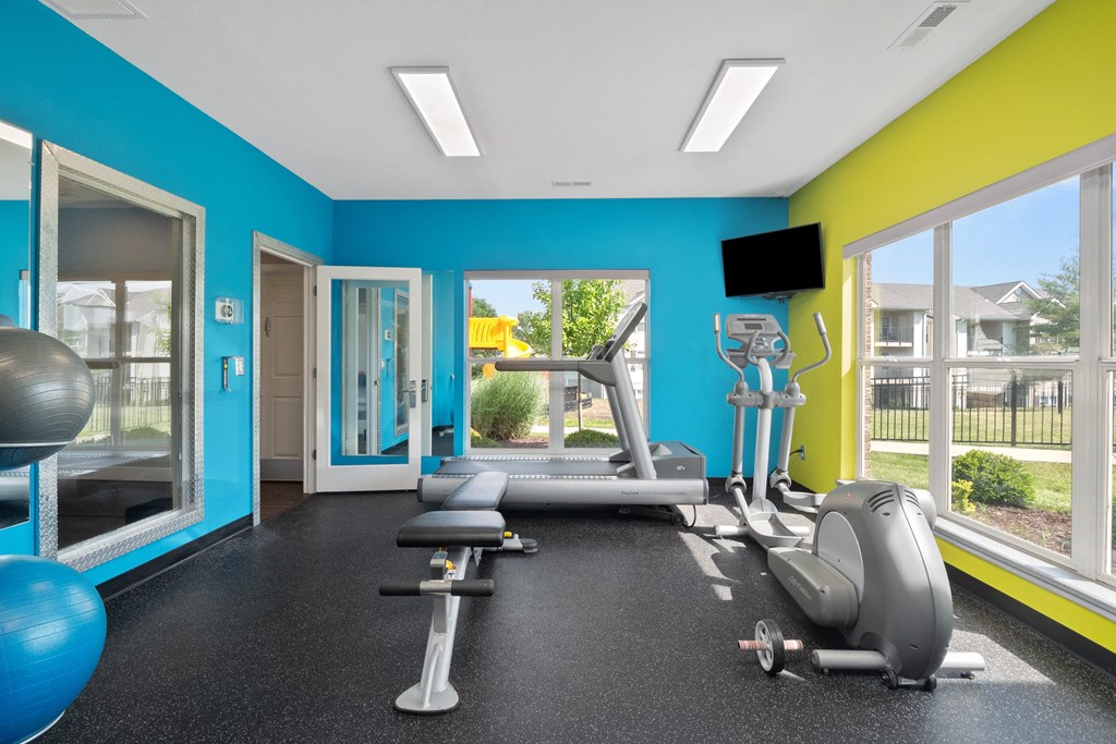 a gym with exercise equipment and windows in a building with blue and yellow walls