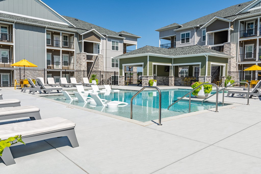 a swimming pool with chaise lounge chairs and sun umbrellas in front of an apartment