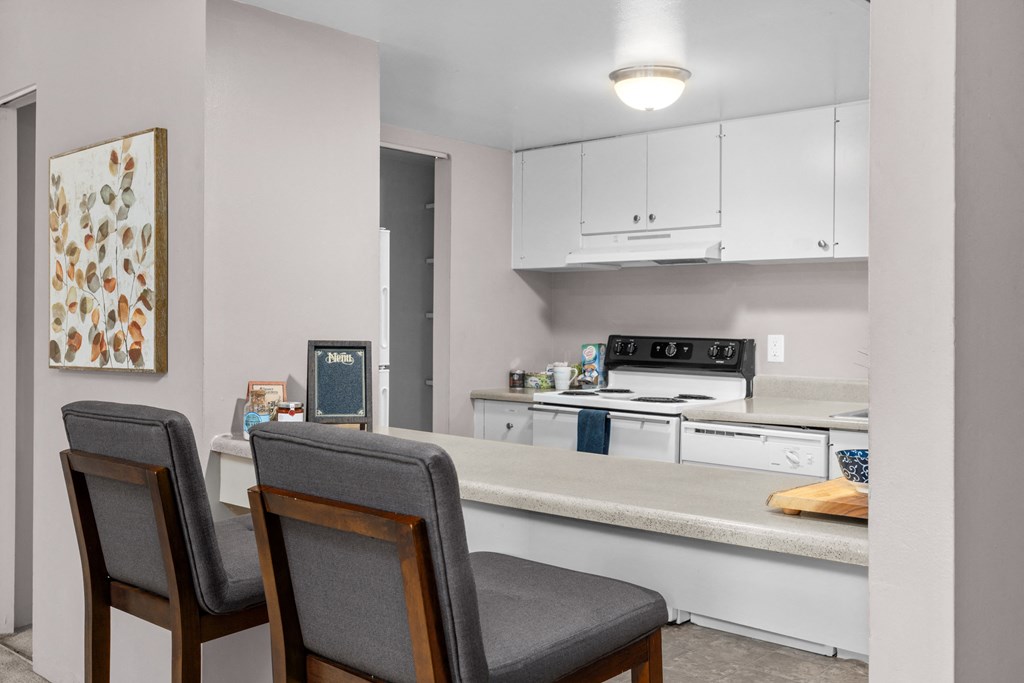 a kitchen with white cabinets and a counter with two chairs