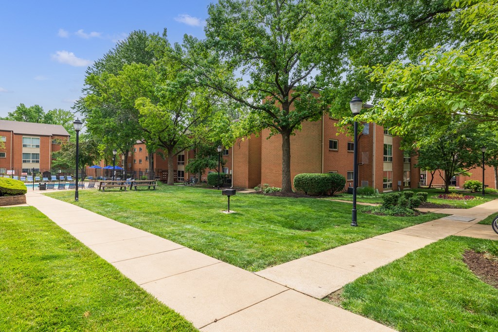 a grassy area with trees and a walkway in front of a brick building