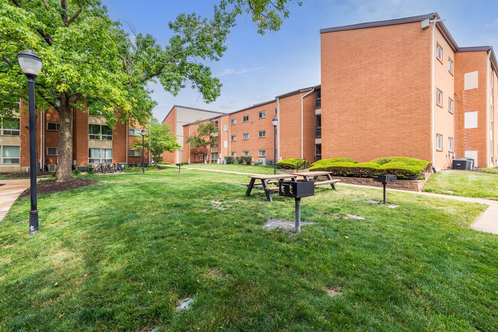 a picnic table and grill sit in a grassy area in front of a brick building