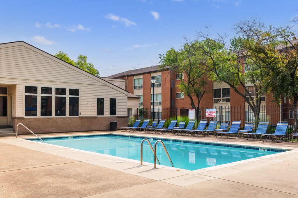 a swimming pool with blue chaise lounge chairs and a brick building in the background