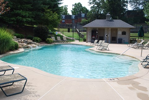 a swimming pool with chairs and a pool house in the background