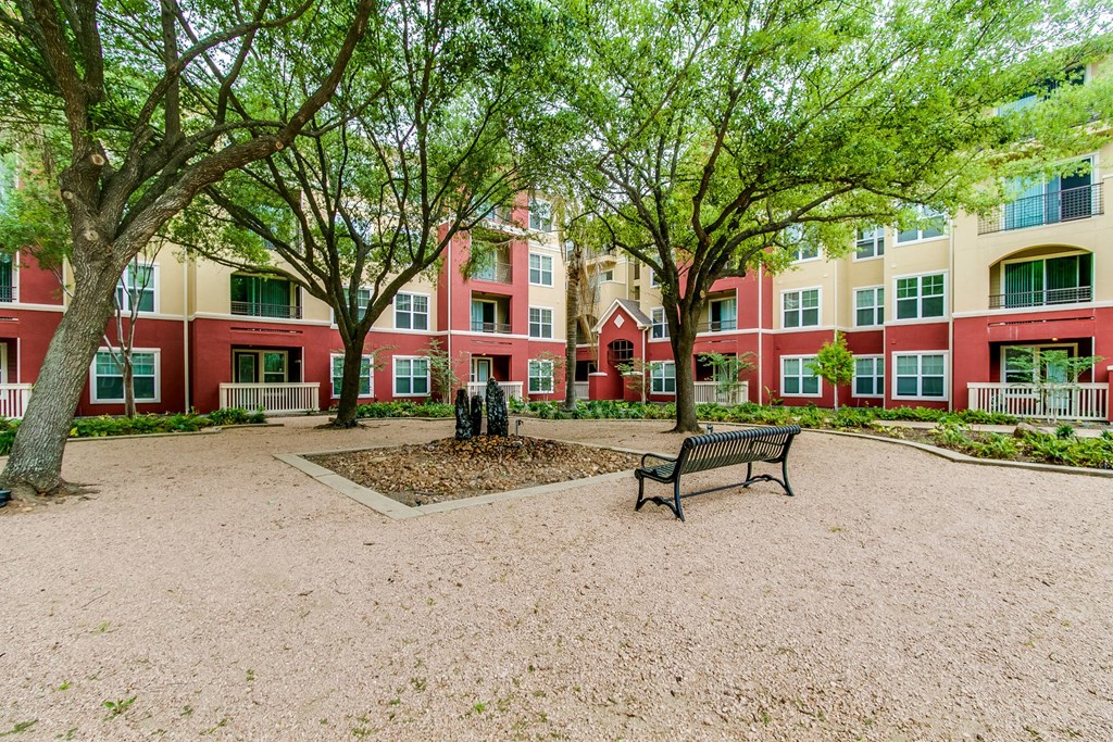 a park with a bench and trees in front of an apartment building