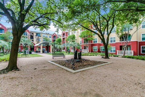 a park with trees and a fountain in front of some apartments
