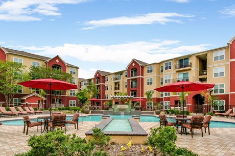 a swimming pool with tables and umbrellas in front of an apartment building