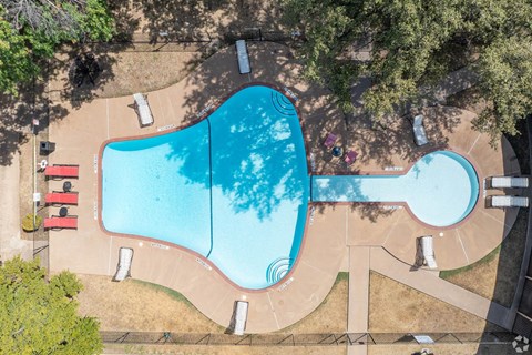 An aerial view of a swimming pool surrounded by trees and a fence.