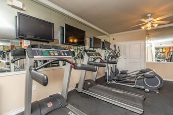 A gym with treadmills, elliptical machines, and a television.