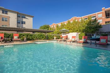 A swimming pool surrounded by red chairs and umbrellas.