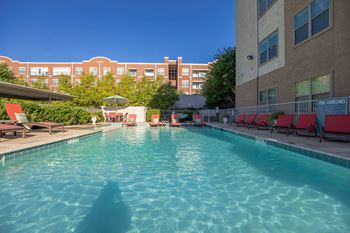 A swimming pool with red sun loungers and a building in the background.