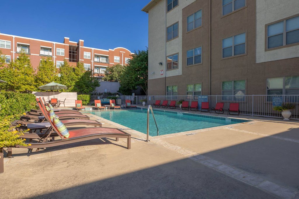 A pool area with chairs and umbrellas in front of a building.