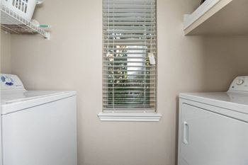 A laundry room with a washer and dryer and a window with blinds.