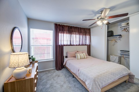 A bedroom with a bed, a nightstand with a lamp, and a ceiling fan.