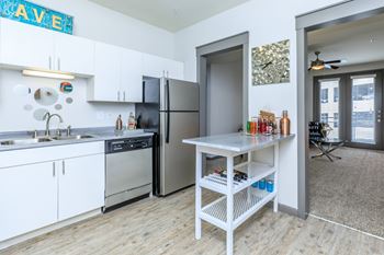 A kitchen with a refrigerator, sink, and a table with bottles on it.