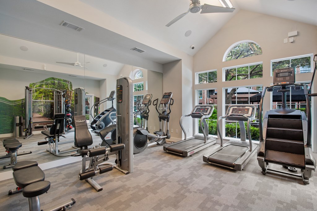 a gym with cardio machines and other exercise equipment in a building with windows