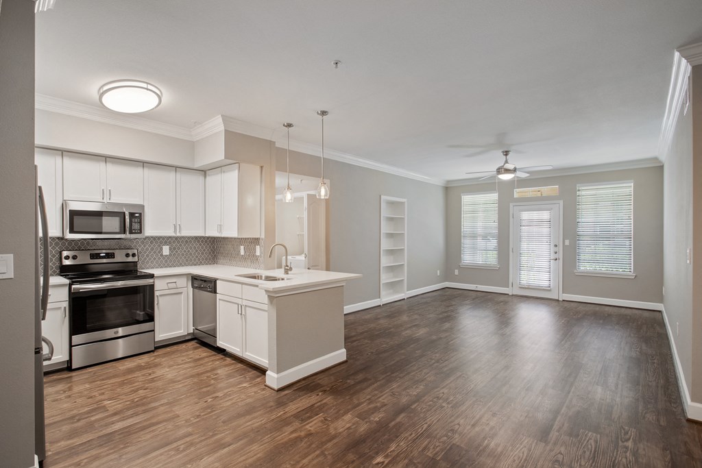 an empty kitchen and living room with wood flooring and white cabinets