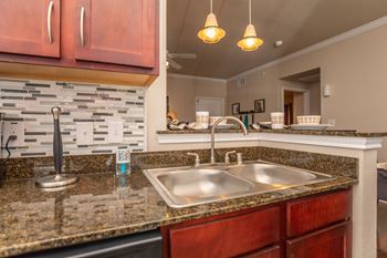 A kitchen with a granite countertop and a stone backsplash.