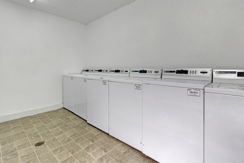 a row of white washers and dryers in an empty laundry room