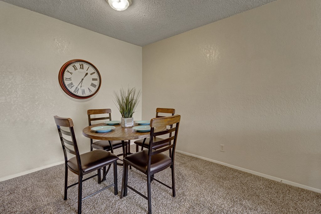 a dining room table with four chairs and a clock on the wall